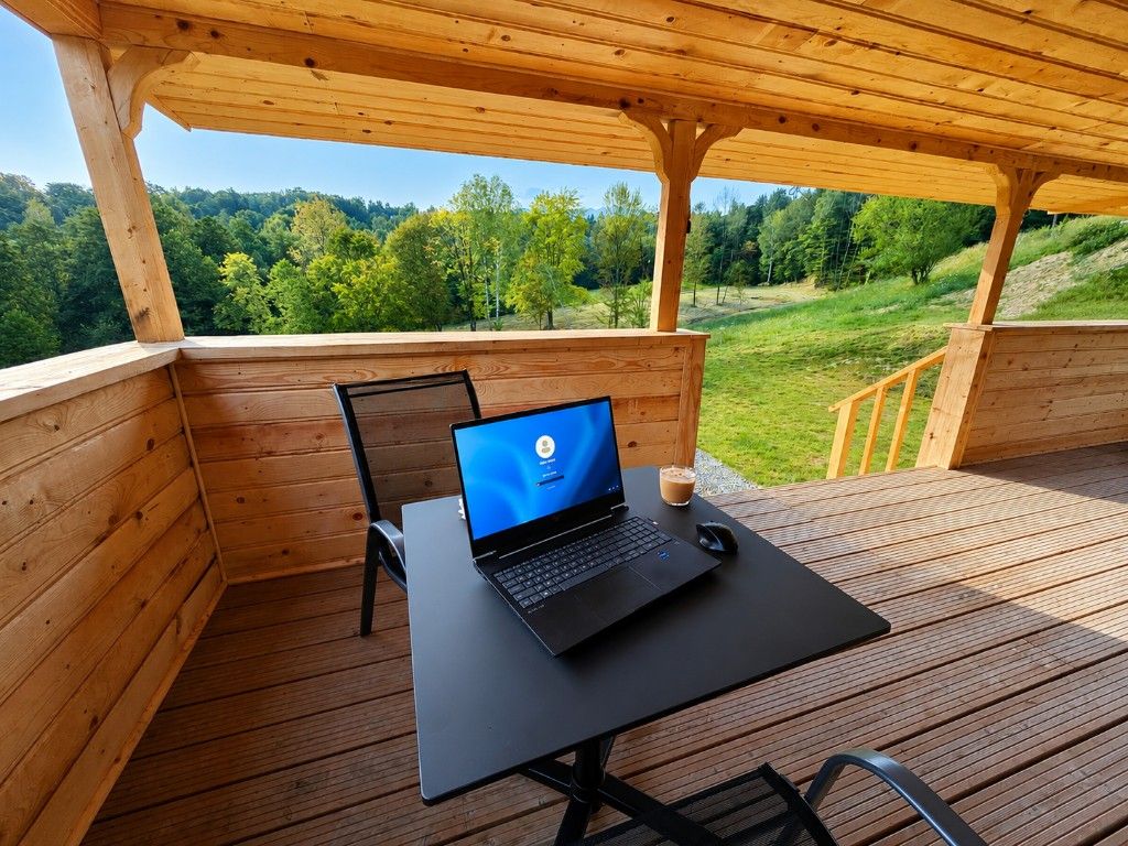 Laptop set up on the covered terrace table, working remotely with a view over the forested valley